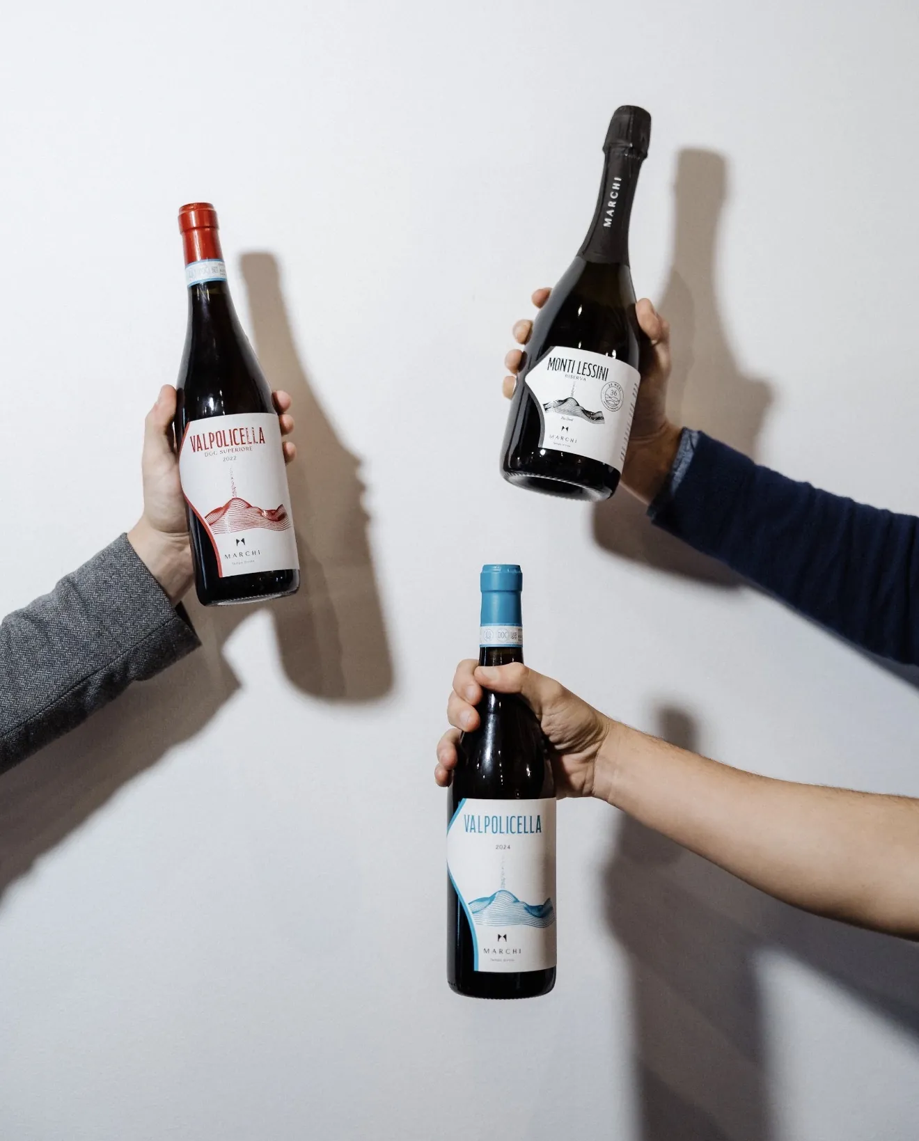 Three hands holding Marchi wine bottles